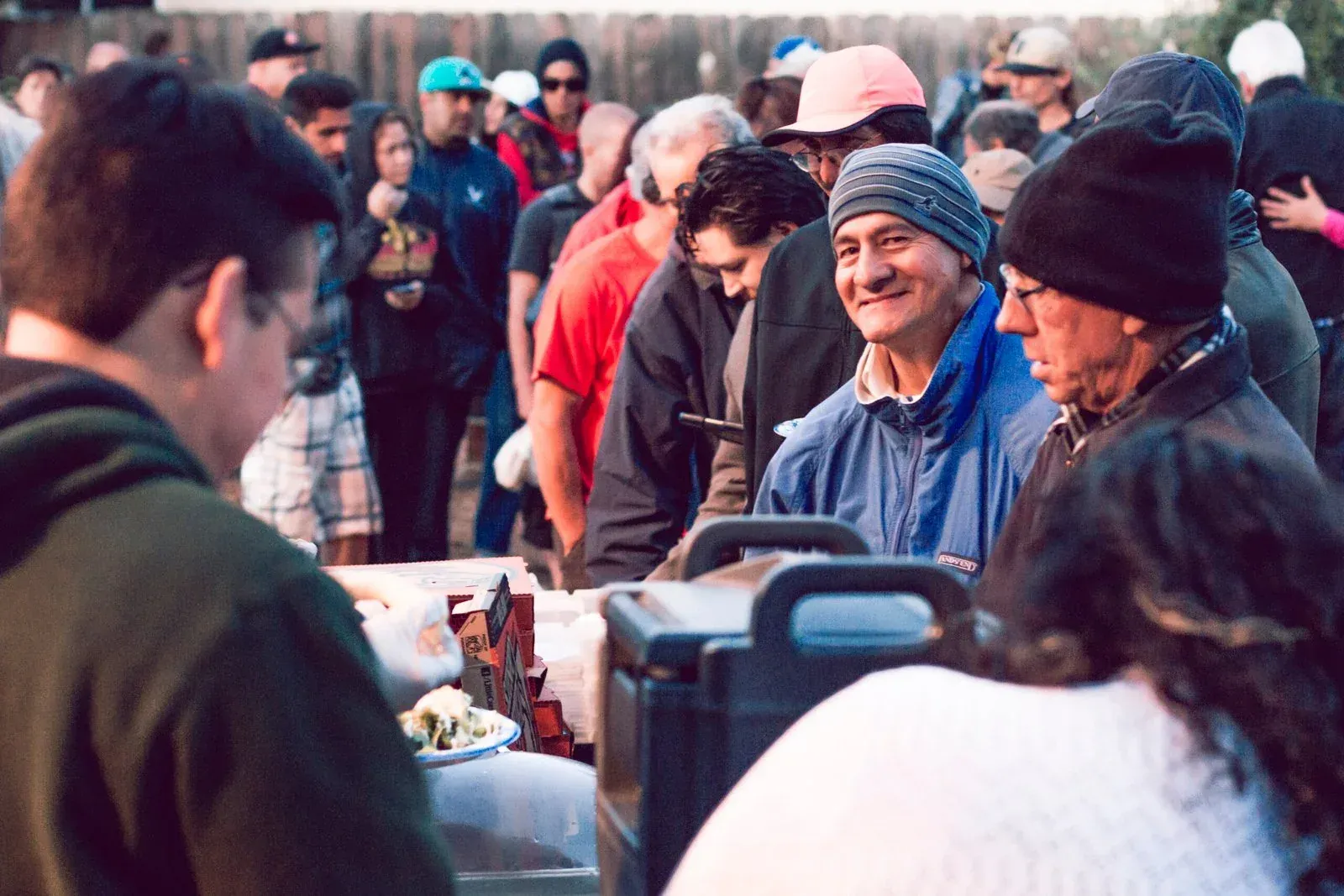 People line up at a Street Life Ministries meal service at golden hour while volunteers serve plates across the table
